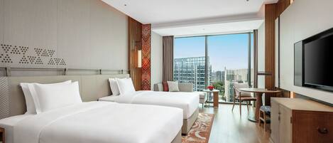 A hotel room with two beds, a TV, a desk, and a view of the city.