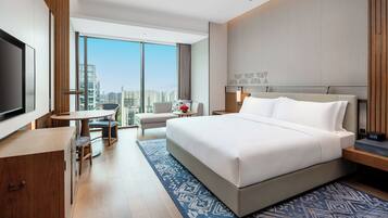 A hotel room with a large bed, a desk, a chair, a TV, and a view of the city.