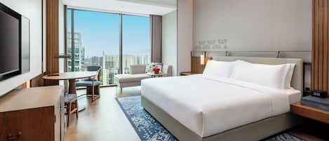 A hotel room with a large bed, a desk, a chair, a TV, and a view of the city.