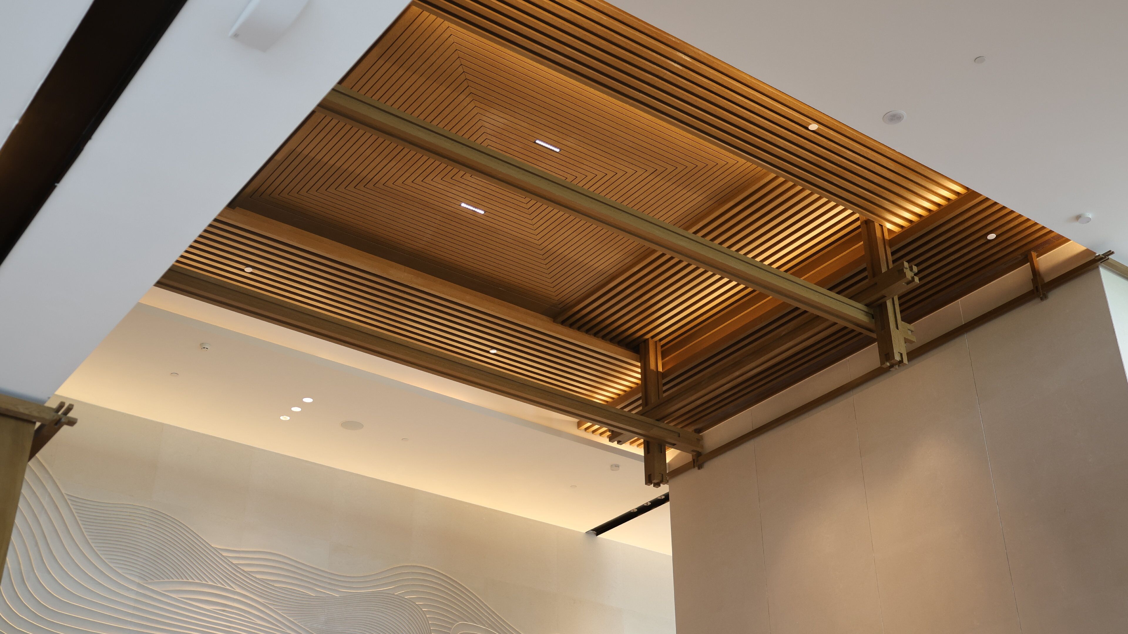 A modern interior with a wooden slatted ceiling, recessed lighting, and a textured wall design.