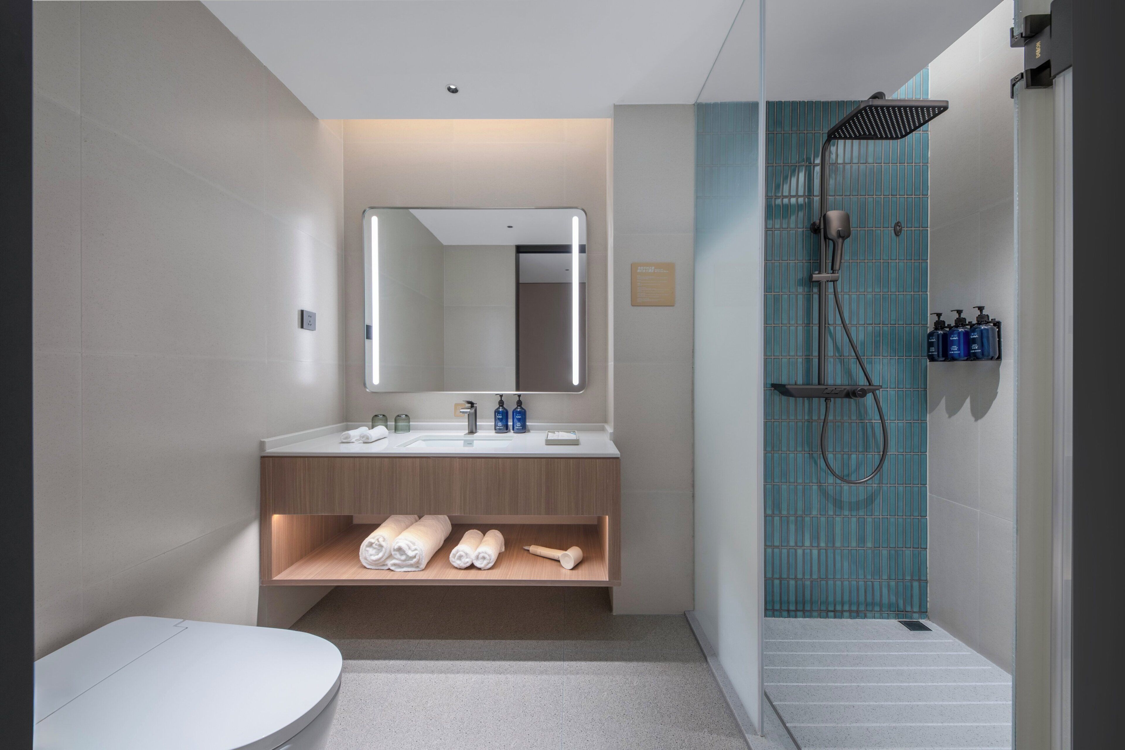 A modern bathroom with a toilet, sink, mirror, shower, and towel storage.