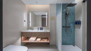 A modern bathroom with a toilet, sink, mirror, shower, and towel storage.
