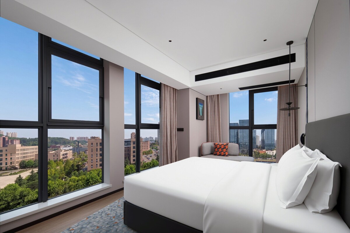 Ein modernes Hotelzimmer mit einem großen Bett und Blick auf die Stadt, inklusive Stadtansicht durch die Fenster.
