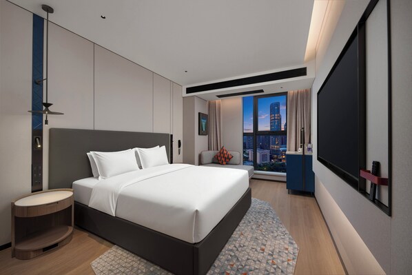 Una habitación de hotel moderna con una cama grande, un área de descanso, un amplio ventanal con vistas a la ciudad y un televisor de pantalla plana.