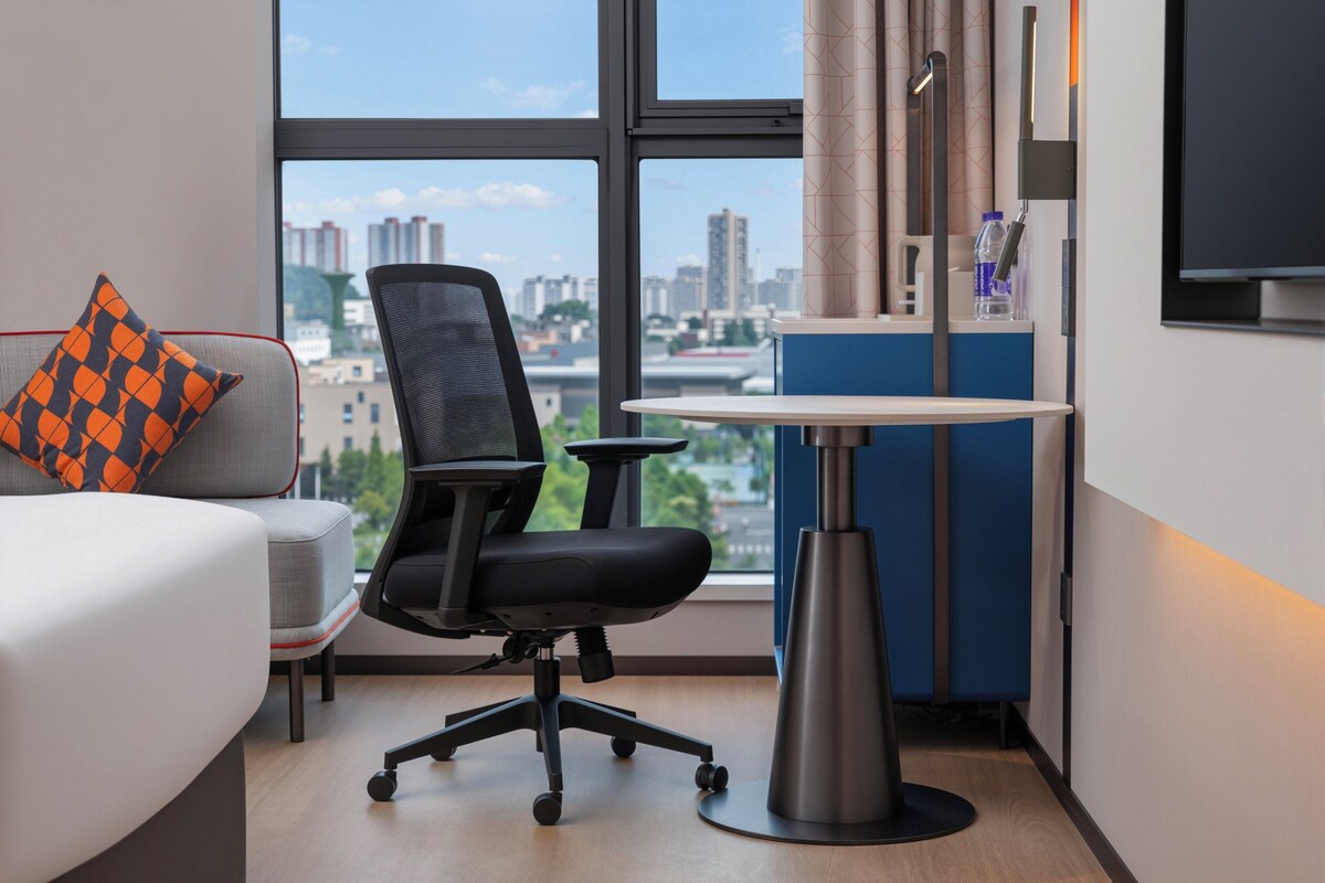 Ein modernes Hotelzimmer mit großem Fenster, Schreibtisch, Stuhl und Bett.