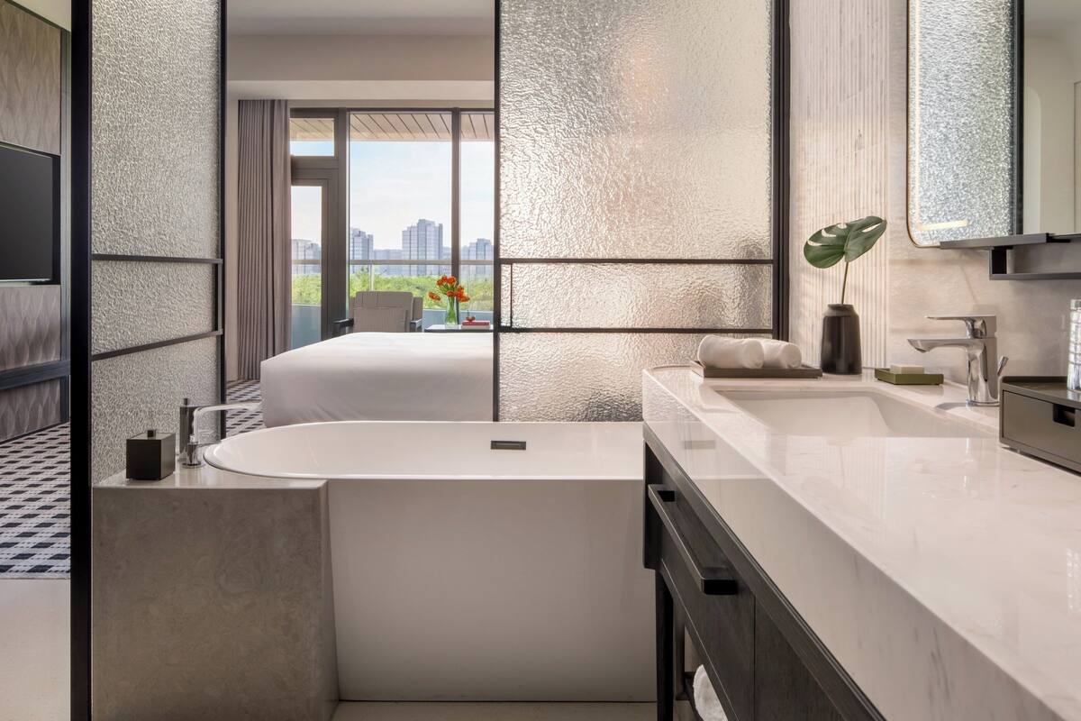 Un baño moderno con bañera, un espejo grande y vistas a un paisaje urbano.