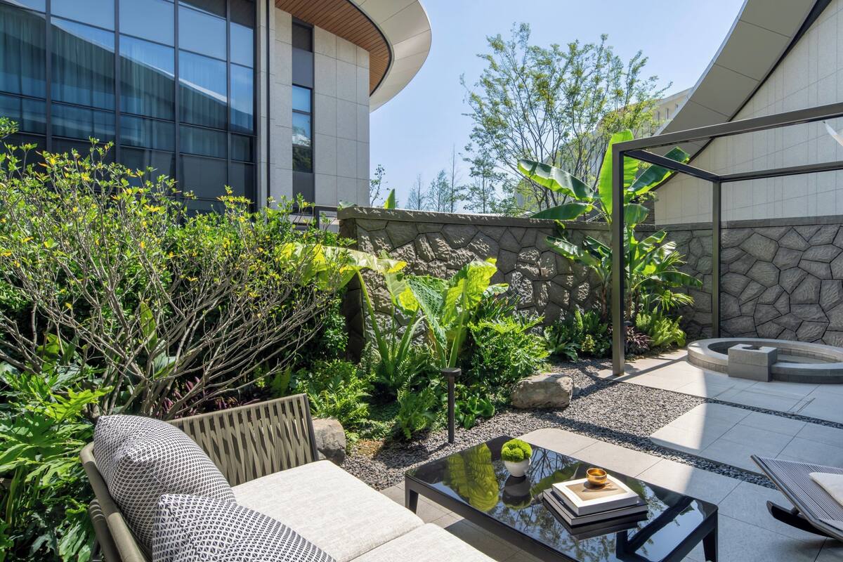 Un patio moderno al aire libre con mobiliario, una mesa de vidrio y un muro de piedra.