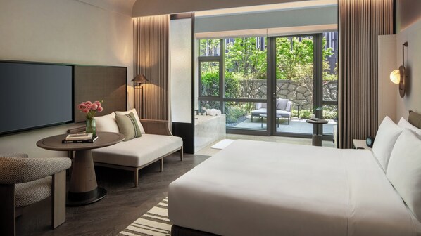 Une chambre d’hôtel avec un lit, un canapé, une télévision, une petite table ornée d’un vase de fleurs et une vue sur l’extérieur.
