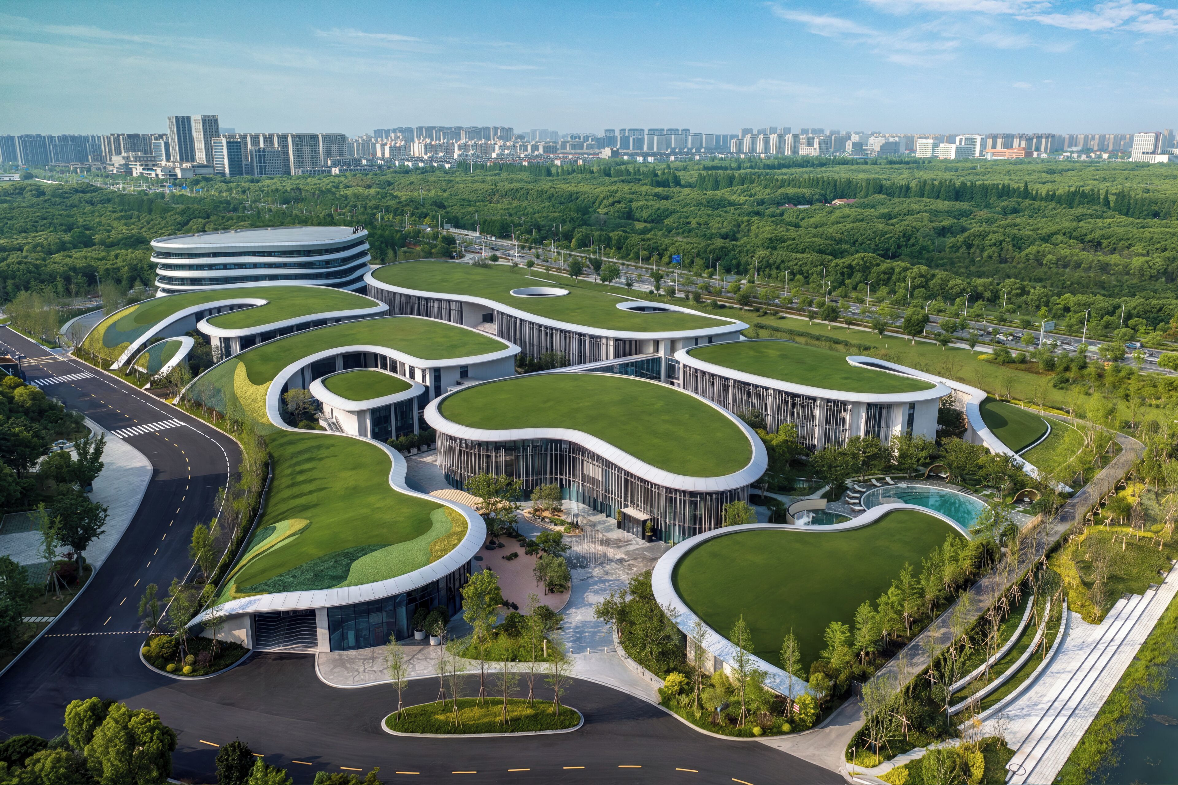 Un edificio moderno con arquitectura curva y techos verdes, rodeado de un área ajardinada con árboles y una carretera.