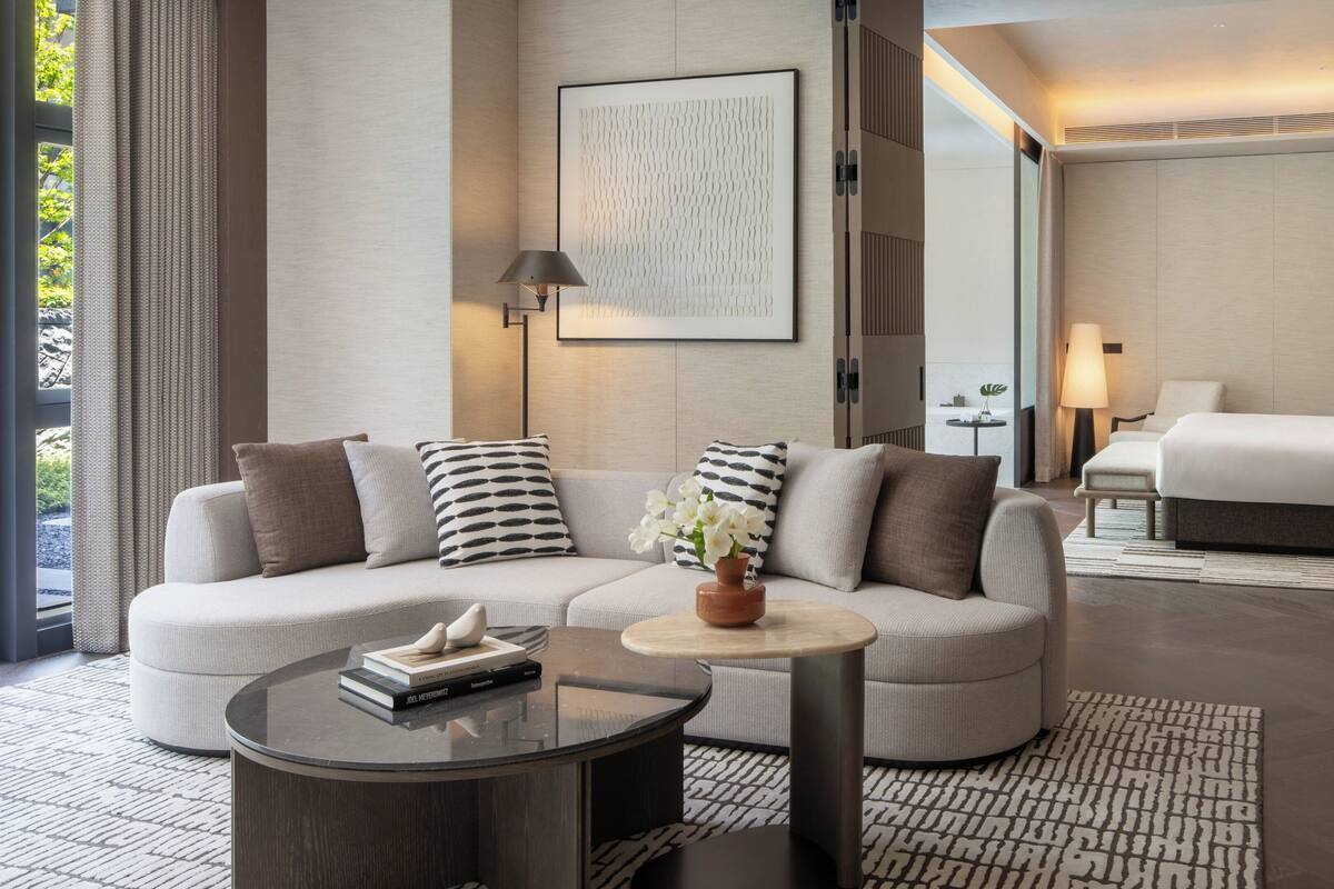 Una habitación de hotel moderna con un sofá, una mesita redonda, una cama y una mesita de noche con lámpara.
