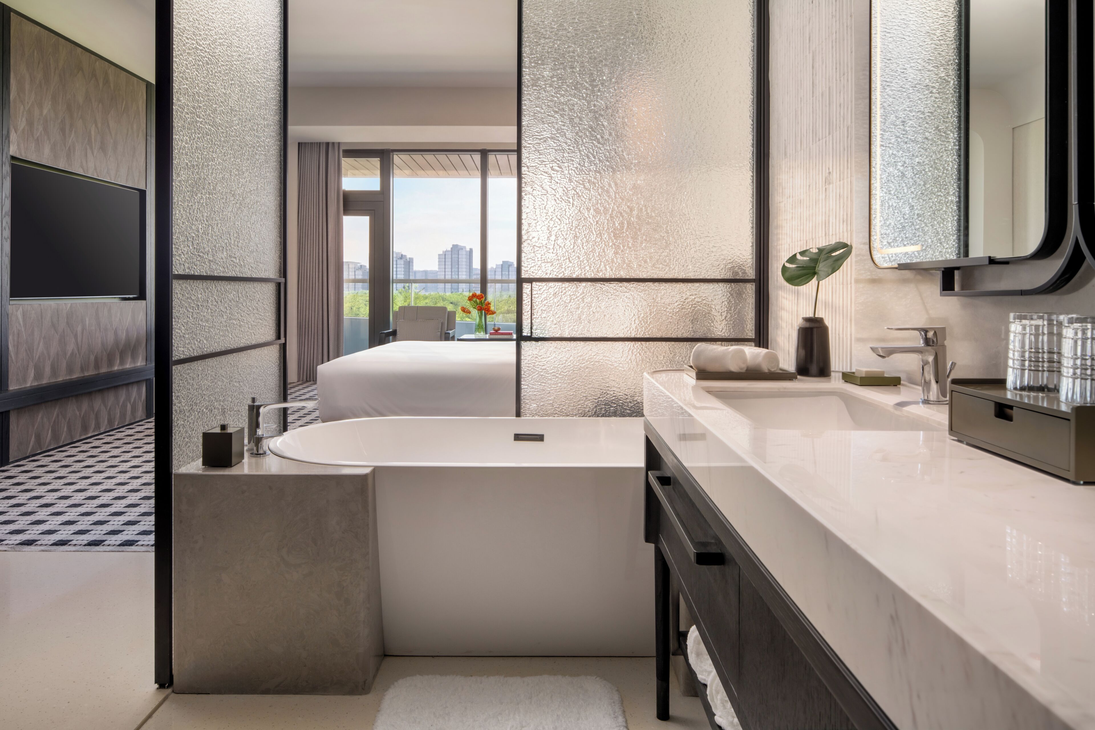 Un baño moderno con una bañera grande, un tocador con espejo y vistas a la ciudad a través de amplias ventanas.
