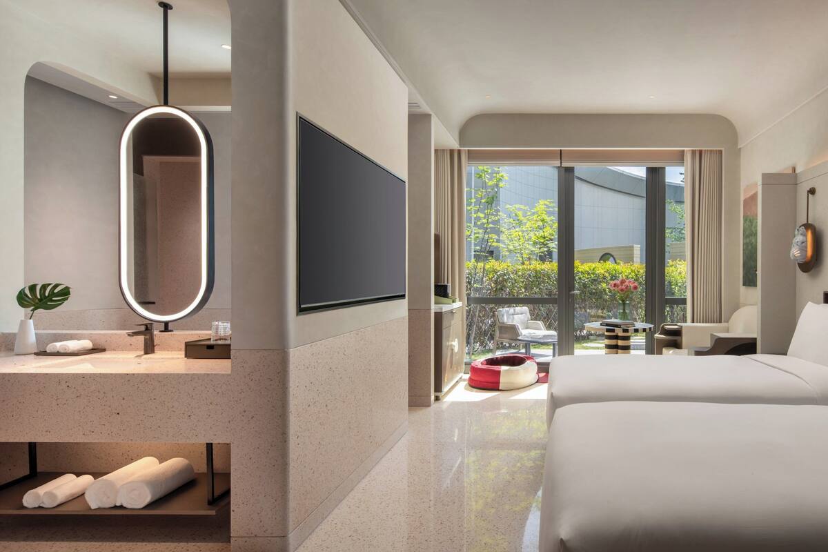 Una habitación de hotel moderna con una cama grande, un televisor, un baño con espejo y vistas a zonas verdes.