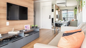 A modern living room with a flat-screen TV, grey entertainment unit, and a sofa with orange cushions. - Expand Pinheiros  (São Paulo)