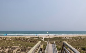 A beach with a wooden boardwalk leading to the water, sandy dunes, and a flag on the beach. - Point Emerald D-104, Oceanview 3BR 3BA Emerald Isle! (Emerald Isle)