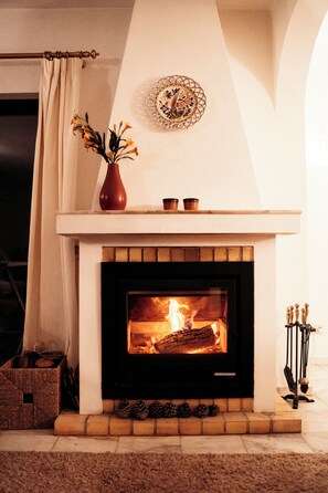 Una chimenea con leña encendida, un jarrón con flores y un plato decorativo en la repisa.
