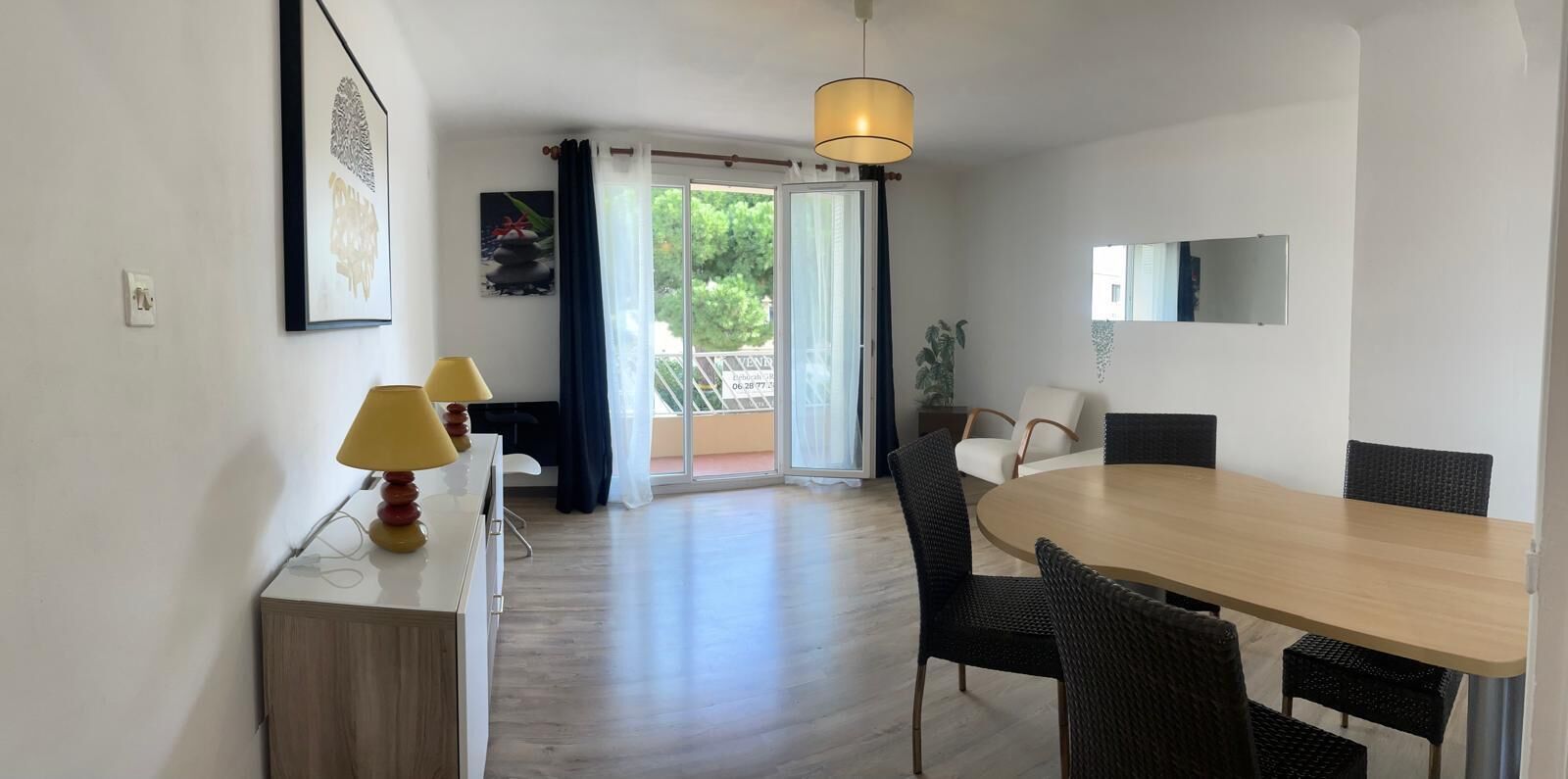 Une chambre moderne équipée d’une table à manger, de chaises, d’une lampe, d’un téléviseur et d’une porte-fenêtre coulissante donnant sur un balcon.