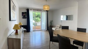 A modern room with a dining table, chairs, a lamp, a TV, and a sliding glass door leading to a balcony. - T3 Sanary-Sur-Mer for rent Holiday 2026 (Sanary-sur-Mer)