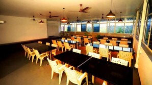A dining area with multiple tables and chairs, ceiling fans, and large windows. - Blueway Residency BusinessBoutique Hotel (Thiruvananthapuram)