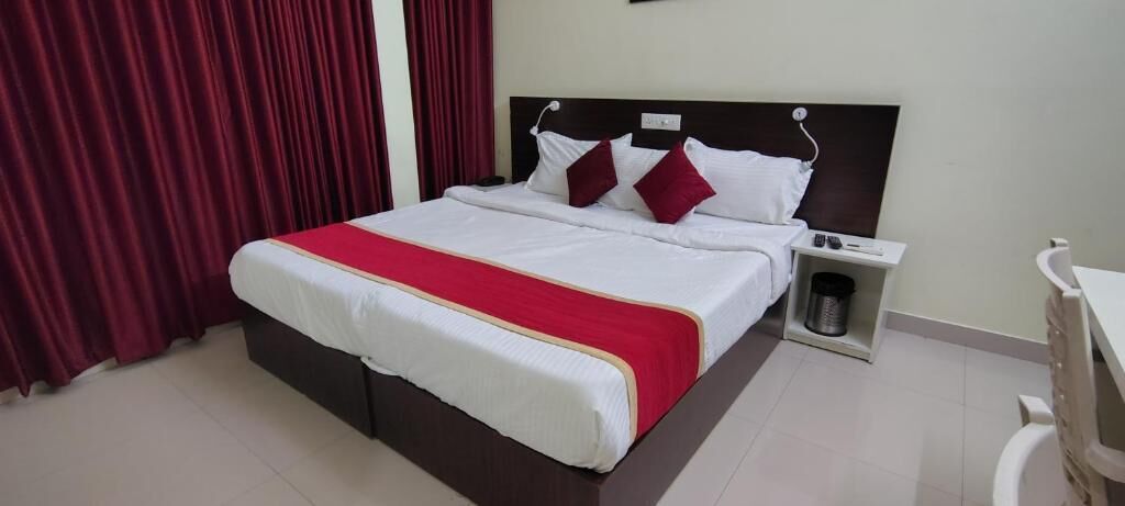 A hotel room with a large bed, a bedside table, a trash bin, and a desk with a chair.