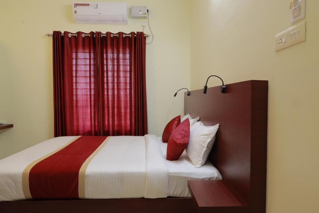Habitación de hotel con cama, cortinas rojas, unidad de aire acondicionado blanca y cabecero marrón.