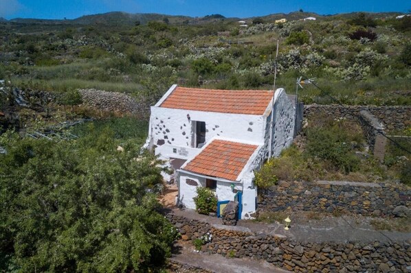 A white building with a red-tiled roof, surrounded by greenery and rocky terrain.