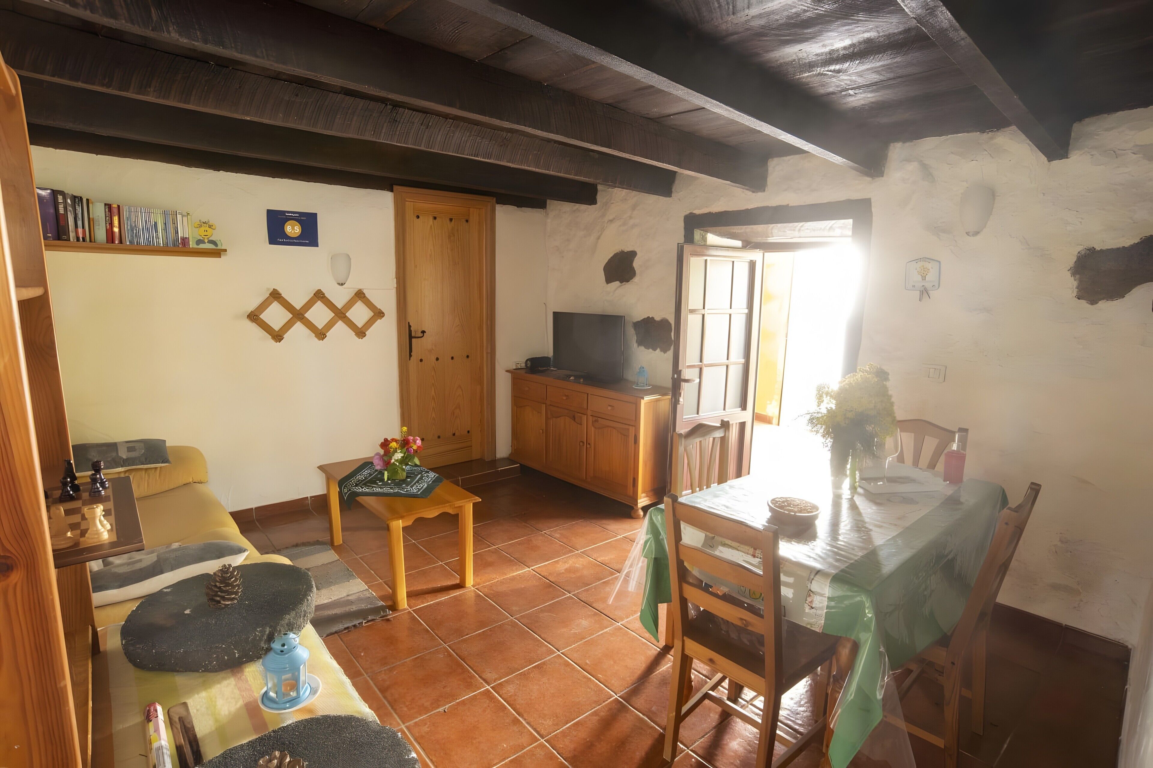 Una sala de estar acogedora con techo de madera, un televisor, una mesa de comedor con sillas y una estantería.