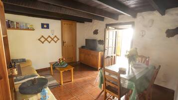 Una sala de estar acogedora con techo de madera, un televisor, una mesa de comedor con sillas y una estantería.