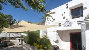 Ein weißes Gebäude mit der Aufschrift 'CASA LOS PASOS GRANDES', einer Terrasse mit Tisch und Stühlen sowie einem großen Sonnensegel.