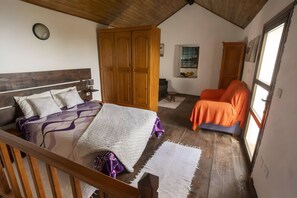 A bedroom with a wooden bed, a wardrobe, an orange chair, and a window with a view.