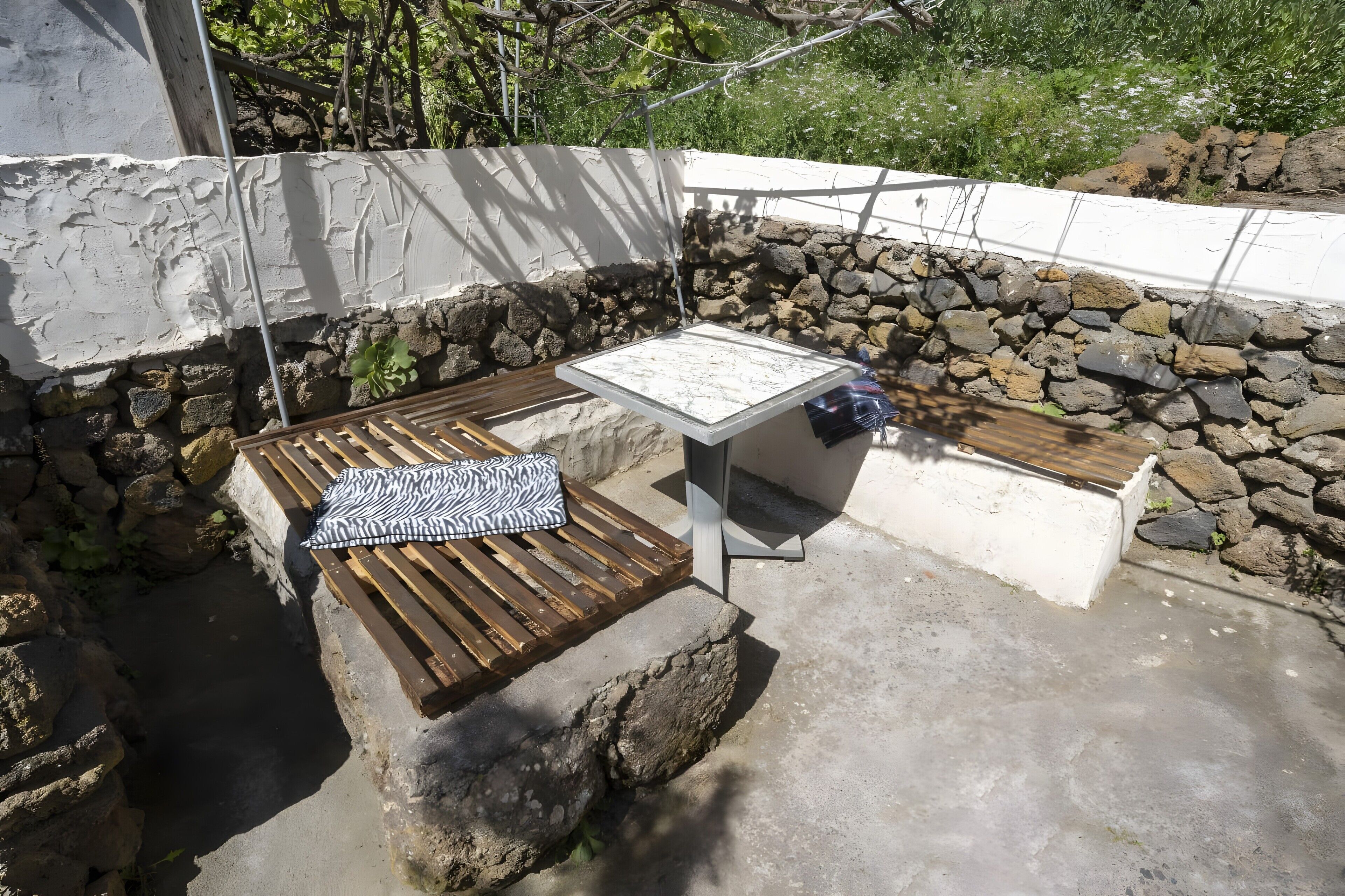 Un área de estar al aire libre con paredes de piedra, un banco de madera y una mesa.