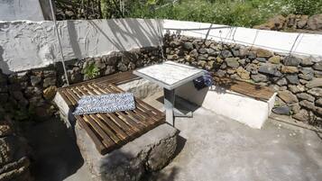 Un área de estar al aire libre con paredes de piedra, un banco de madera y una mesa.