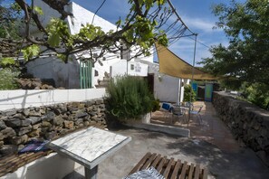 A patio with a table and chairs, a stone wall, and a building with a white facade and green door.