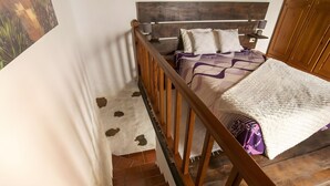 Ein Schlafzimmer mit Holz-Kopfteil, einem Bett mit gemusterten Bettbezügen, einem weißen Teppich und einer Holztreppe.