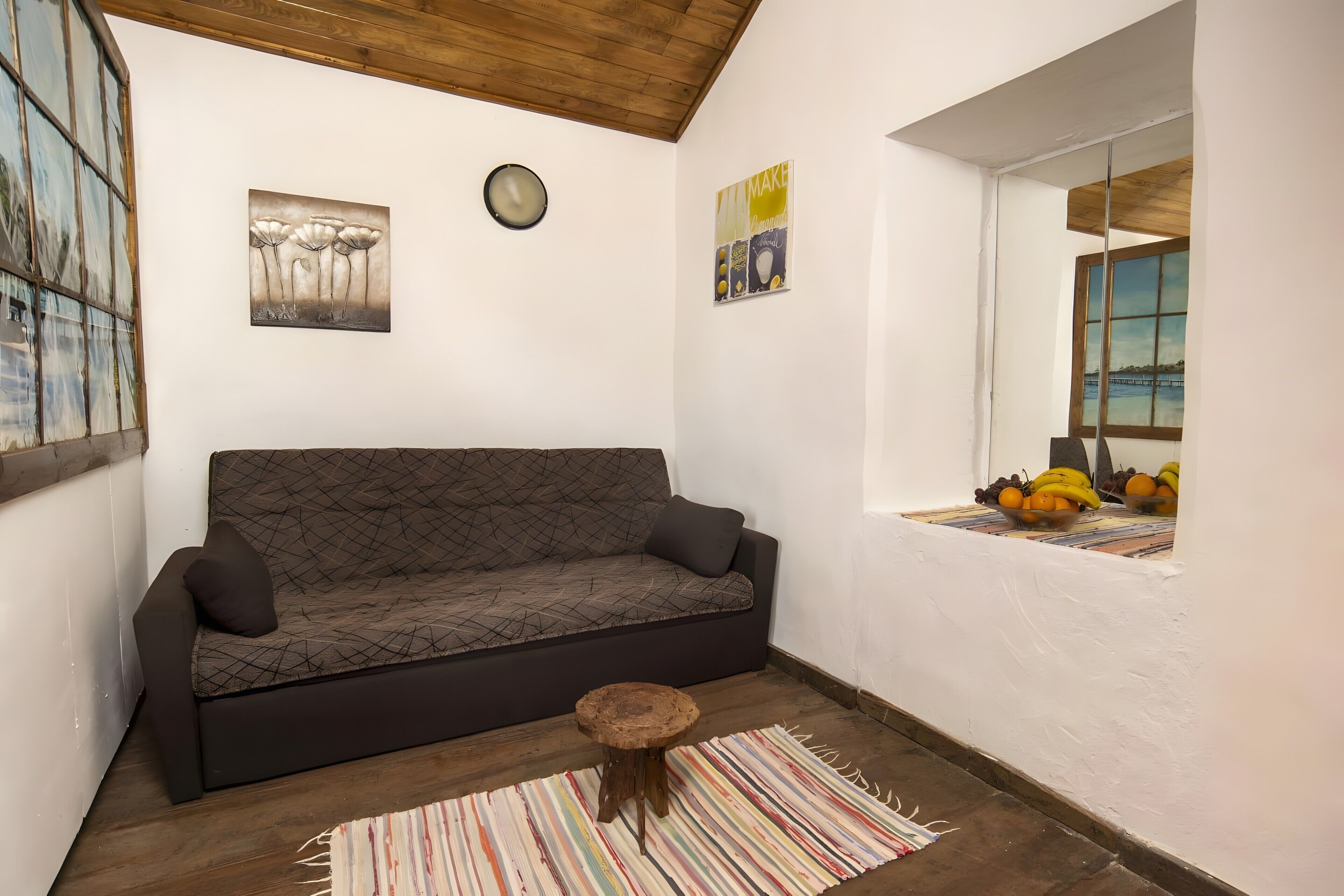 A cozy room with a sofa, a small wooden stool, and a window with fruit.