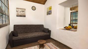 Ein gemütliches Zimmer mit einer Couch, einem kleinen Holzschemel und einem Fenster mit Obst.