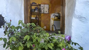 Ein rustikaler Raum mit einer Holztür, einem Regal mit verschiedenen Gegenständen und einem kleinen Fenster mit einer Pflanze im Vordergrund.