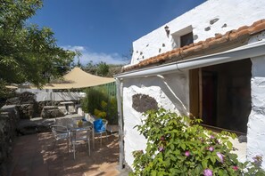 A white building with a tiled roof, a patio with chairs, and a table.