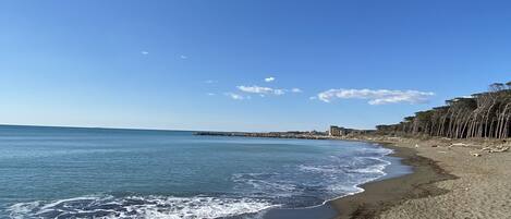A beach with clear blue water, a sandy shore, and a distant pier.