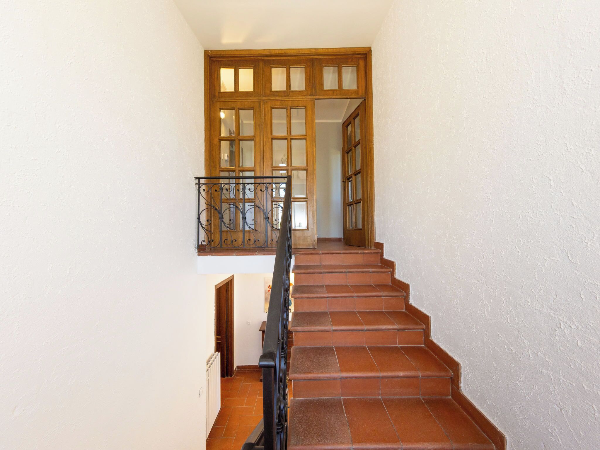 Una escalera con barandilla metálica que conduce a una puerta de madera con paneles de vidrio.