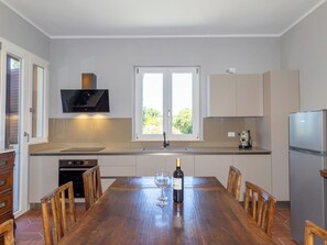 Una cocina moderna con una mesa de comedor, sillas, una botella de vino y un televisor.