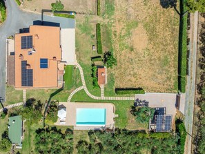 Vista aérea de una propiedad residencial con piscina, paneles solares y césped cuidado.