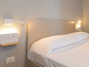 Ein Hotelzimmer mit Bett, Nachttisch, Steckdose und Wandleuchte.