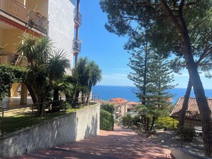 A residential area with a view of the sea, a paved pathway, and a building with balconies. - Titti e Giba by Interhome (Costarainera)