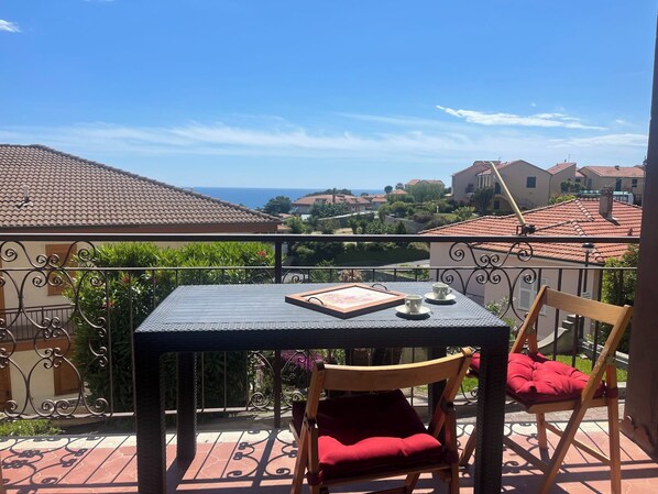 En balkon med et bord, stole og havudsigt samt huse.