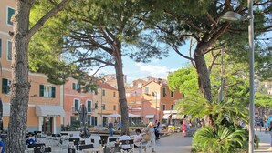 An outdoor cafe with tables and chairs, surrounded by trees and buildings. - casa JS by Interhome (Imperia)