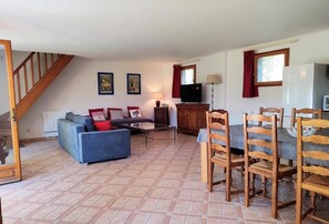 A living room with a sofa, chairs, a TV, a wooden cabinet, and a dining table.