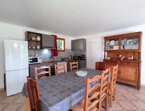 A compact kitchen with a dining table, chairs, a refrigerator, microwave, and a cabinet with dishes.
