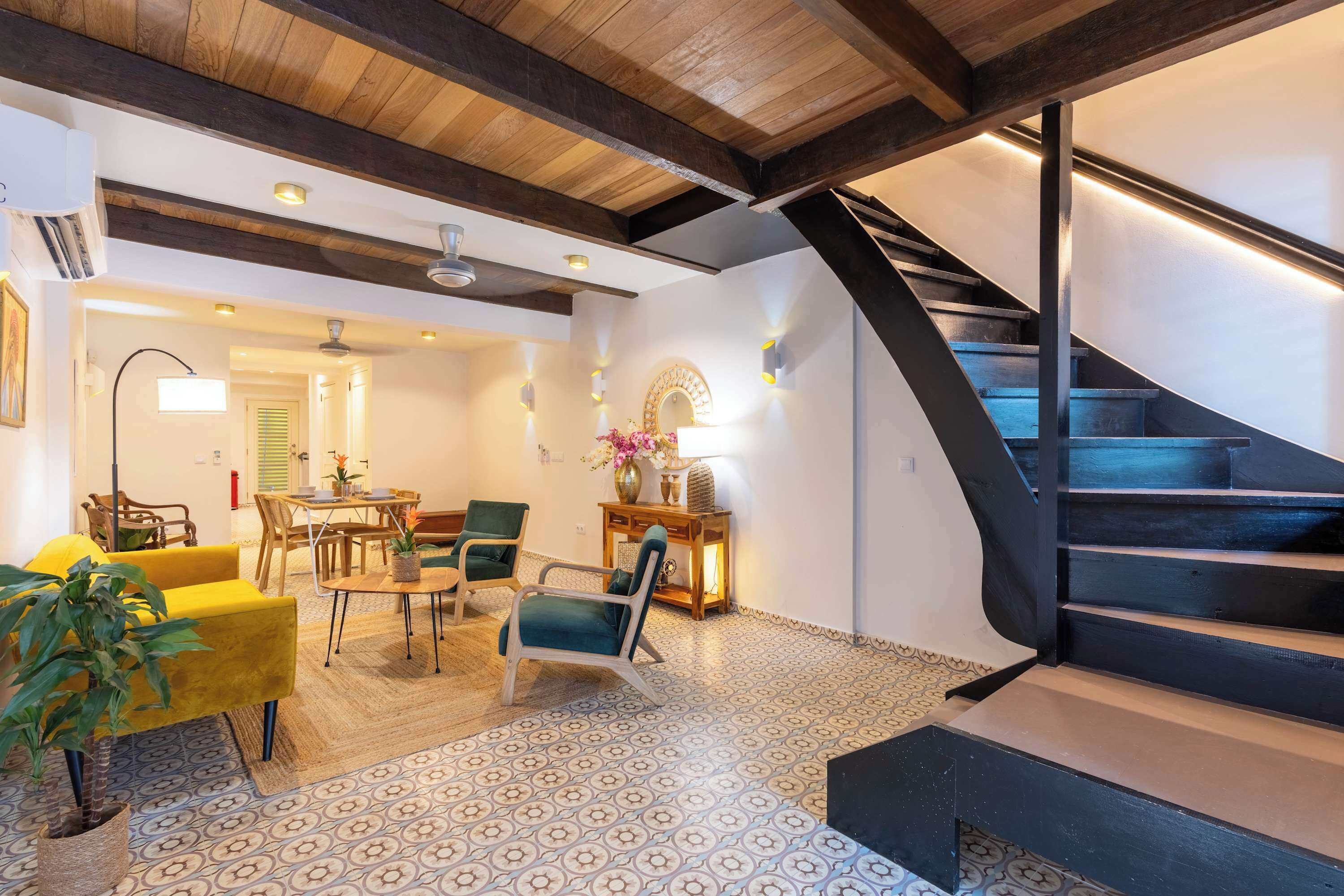 A modern interior with a staircase, wooden beams, patterned flooring, and a dining area with chairs and a table.