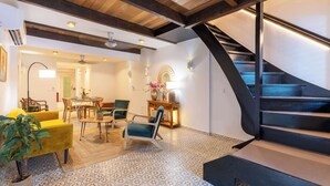 Interior moderno com escada, vigas de madeira, piso estampado e sala de jantar com cadeiras e mesa.