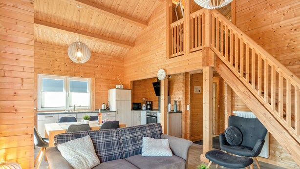 Et interiør af en træhytte med sofa, spisebord, køkken og trappe.